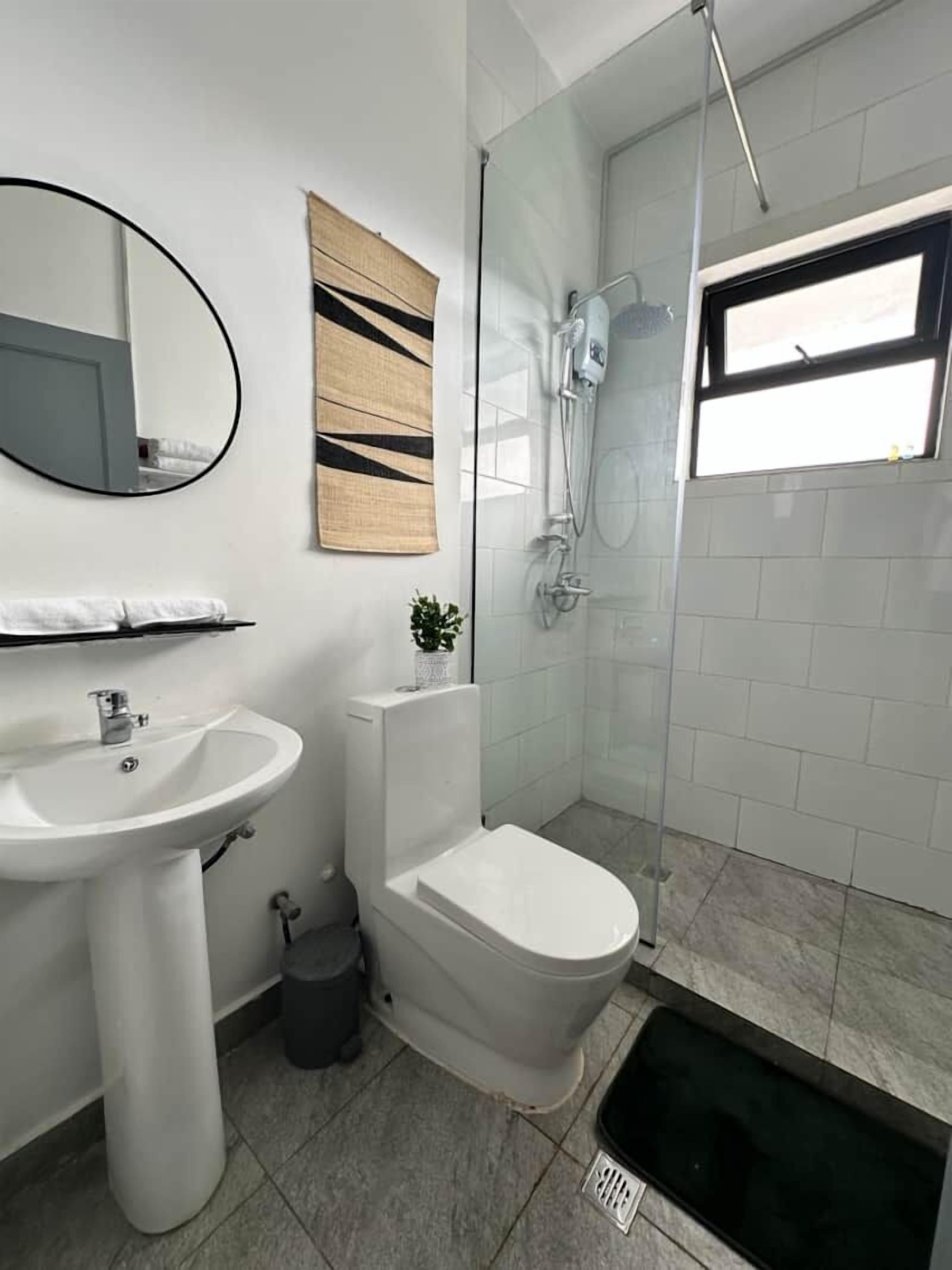 A modern bathroom with a white sink, toilet, and shower. There is a mirror, a towel rack, and a small plant.