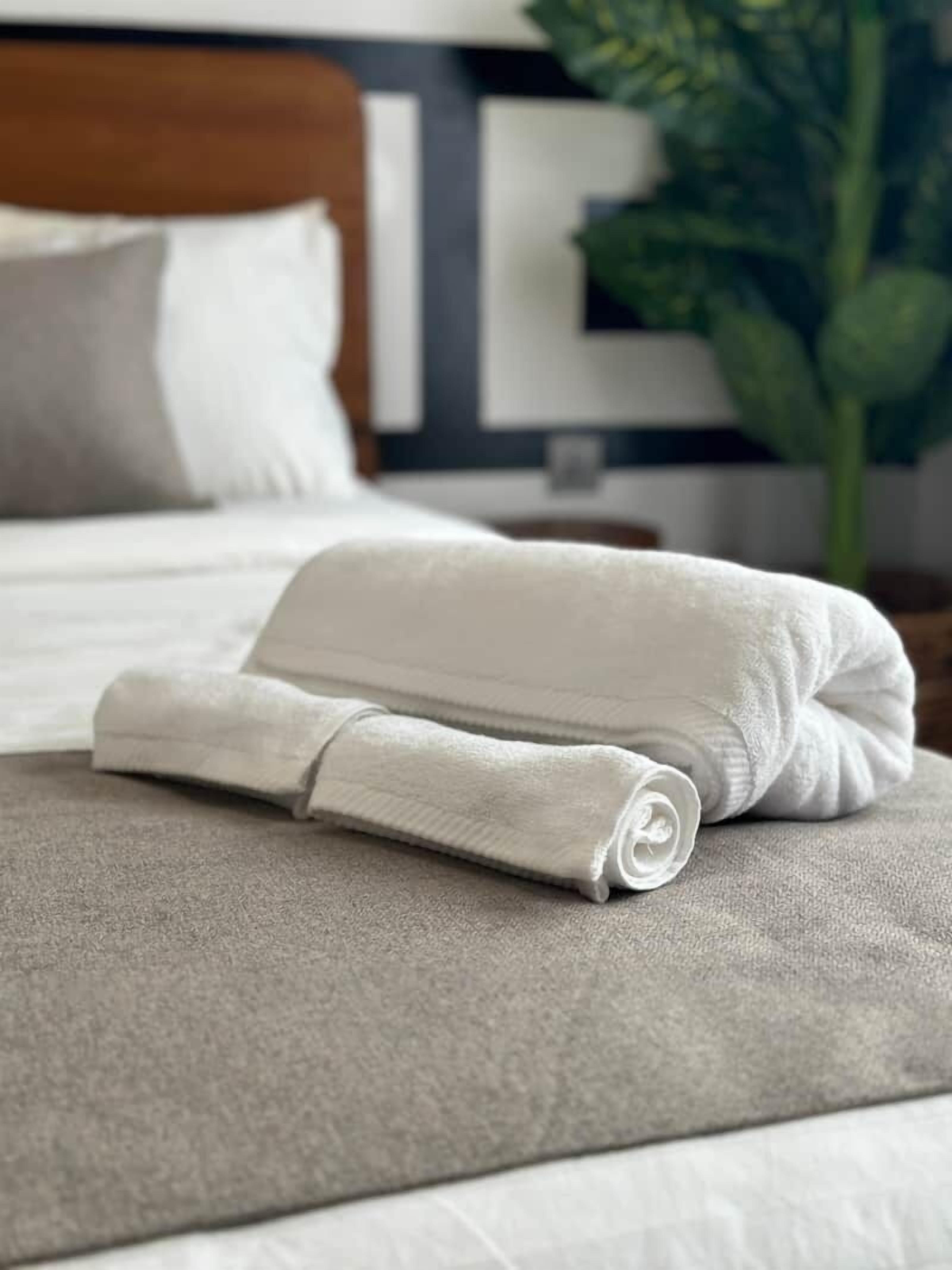 A neatly folded white towel on a beige bed in a hotel room.