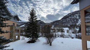 A snowy landscape with a mountain backdrop, a snow-covered ground, and a building with a balcony. - Spacious apartment 8 guests, south-facing balcony, parking (La Salle-les-Alpes)