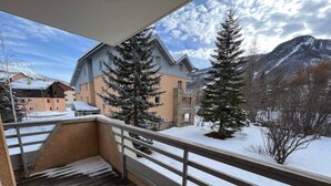 A balcony with a wooden floor and metal railing, overlooking a snowy landscape with buildings and mountains. - Spacious apartment 8 guests, south-facing balcony, parking (La Salle-les-Alpes)