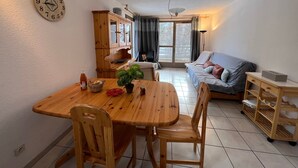 A cozy living room with a wooden dining table, chairs, a sofa, and a large window. - Spacious apartment 8 guests, south-facing balcony, parking (La Salle-les-Alpes)