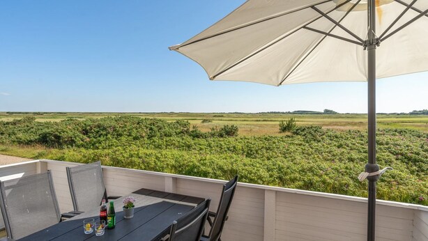 An outdoor patio with a table and chairs, a large umbrella, and a view of a field. - "Maura" - 2.3km from the sea by Interhome (Rømø)