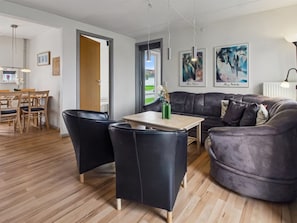 Una sala moderna con un sofá de cuero oscuro, una mesa de centro de madera y un comedor con una mesa y sillas de madera.