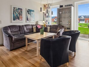 En moderne stue med en lædersofa, et træsofabord og sorte stole. Der er abstrakte malerier på væggen og et glaskab med pynteting.