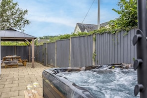 A hot tub with a wooden deck and a picnic table in a backyard.