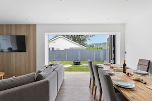 A modern living room with a sofa, a dining table set for four, and a TV mounted on the wall.