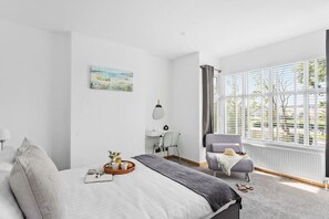 A bedroom with a large bed, a chair, a window with blinds, and a painting on the wall.