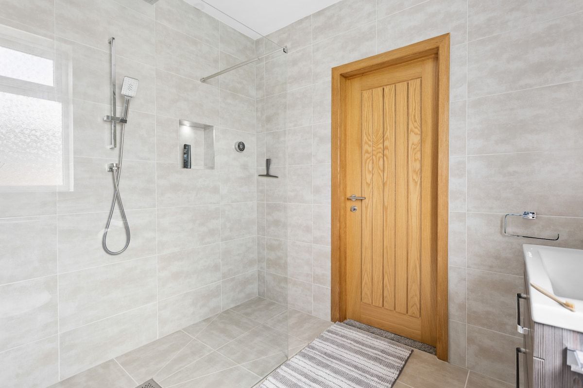 Une salle de bain moderne avec une douche, une porte en bois et un lavabo blanc.