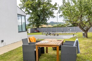 An outdoor seating area with a table and chairs, a tree, and a view of a sports field.