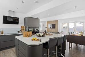 A modern kitchen with a central island, bar stools, and a dining area with a large window.