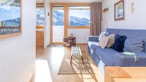 Una sala de estar acogedora con un sofá azul, una mesa de centro de madera y vistas a montañas nevadas a través de amplios ventanales.