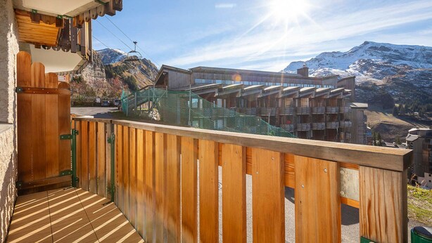 Un balcón de madera con vistas a un paisaje montañoso y un edificio con varios balcones.
