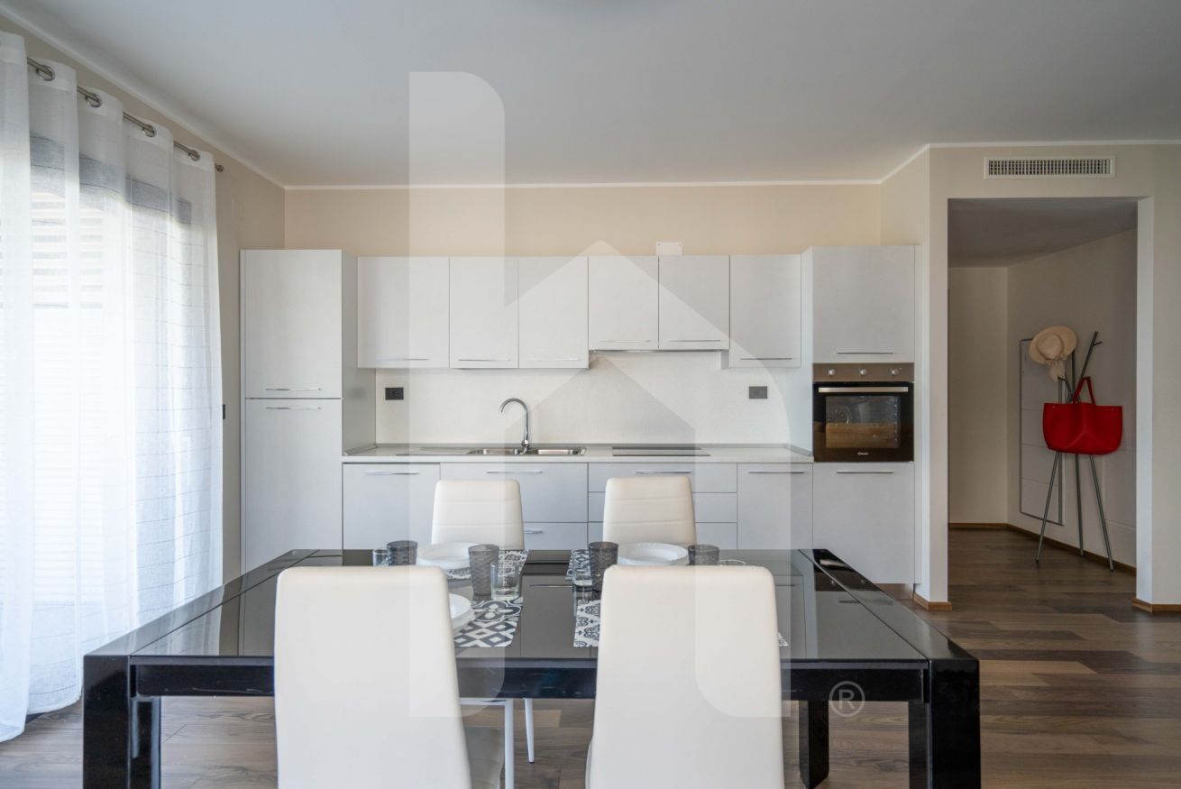 Une cuisine moderne avec des meubles blancs, une table à manger en verre et une chaise rouge.