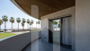 A modern building with a curved balcony overlooking a beach with palm trees.