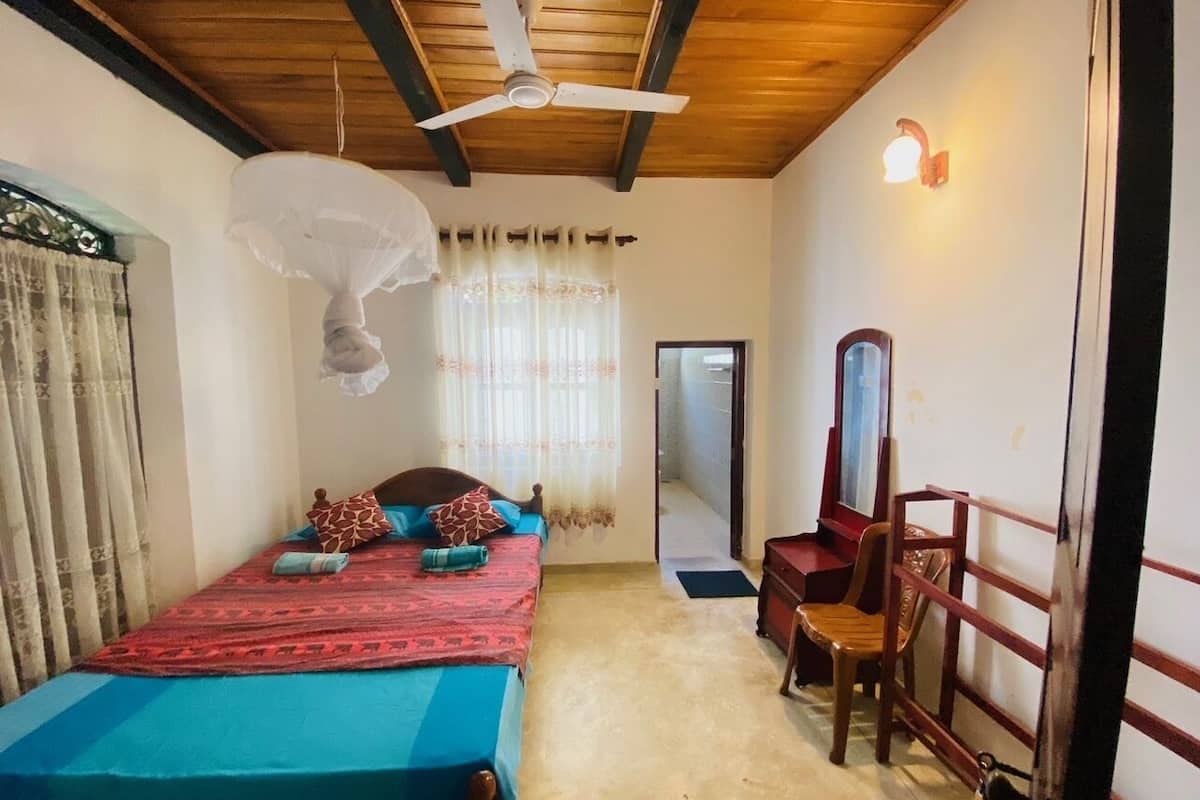 A bedroom with a bed, a chair, a ceiling fan, a window with curtains, and a door.