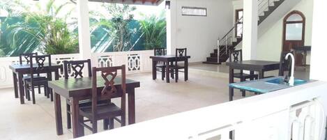 A covered outdoor seating area with tables and chairs, a pool table, and a staircase leading to an upper level.