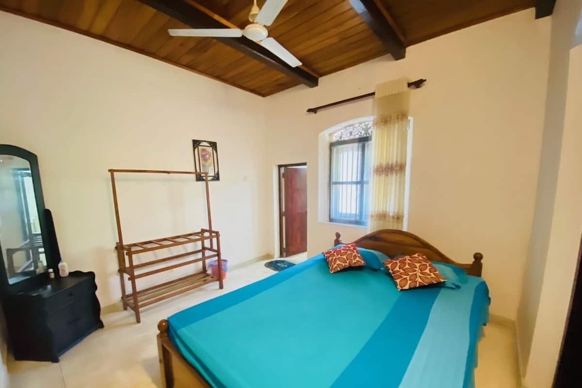 A bedroom with a bed, a wooden ladder, a mirror, and a window with curtains.