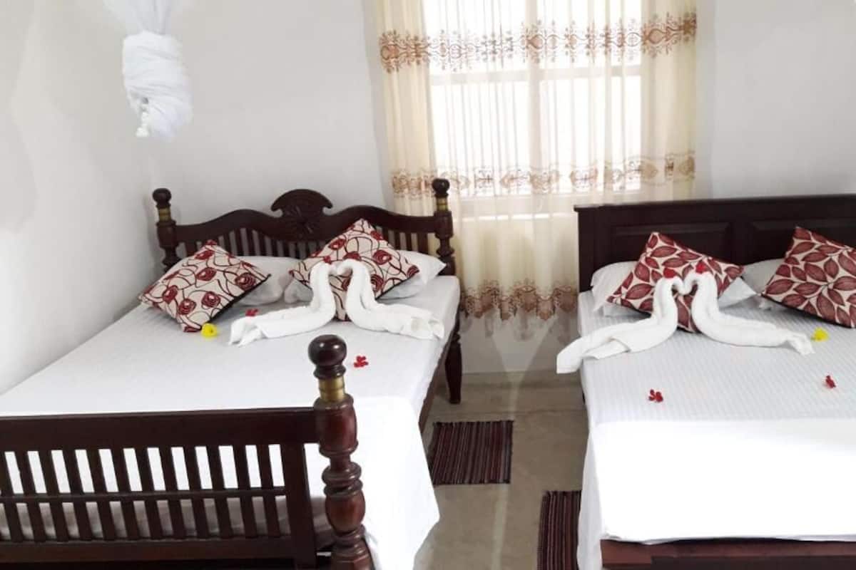 Two wooden beds with white bedding and red patterned pillows, a window with sheer curtains, and a white hanging canopy.