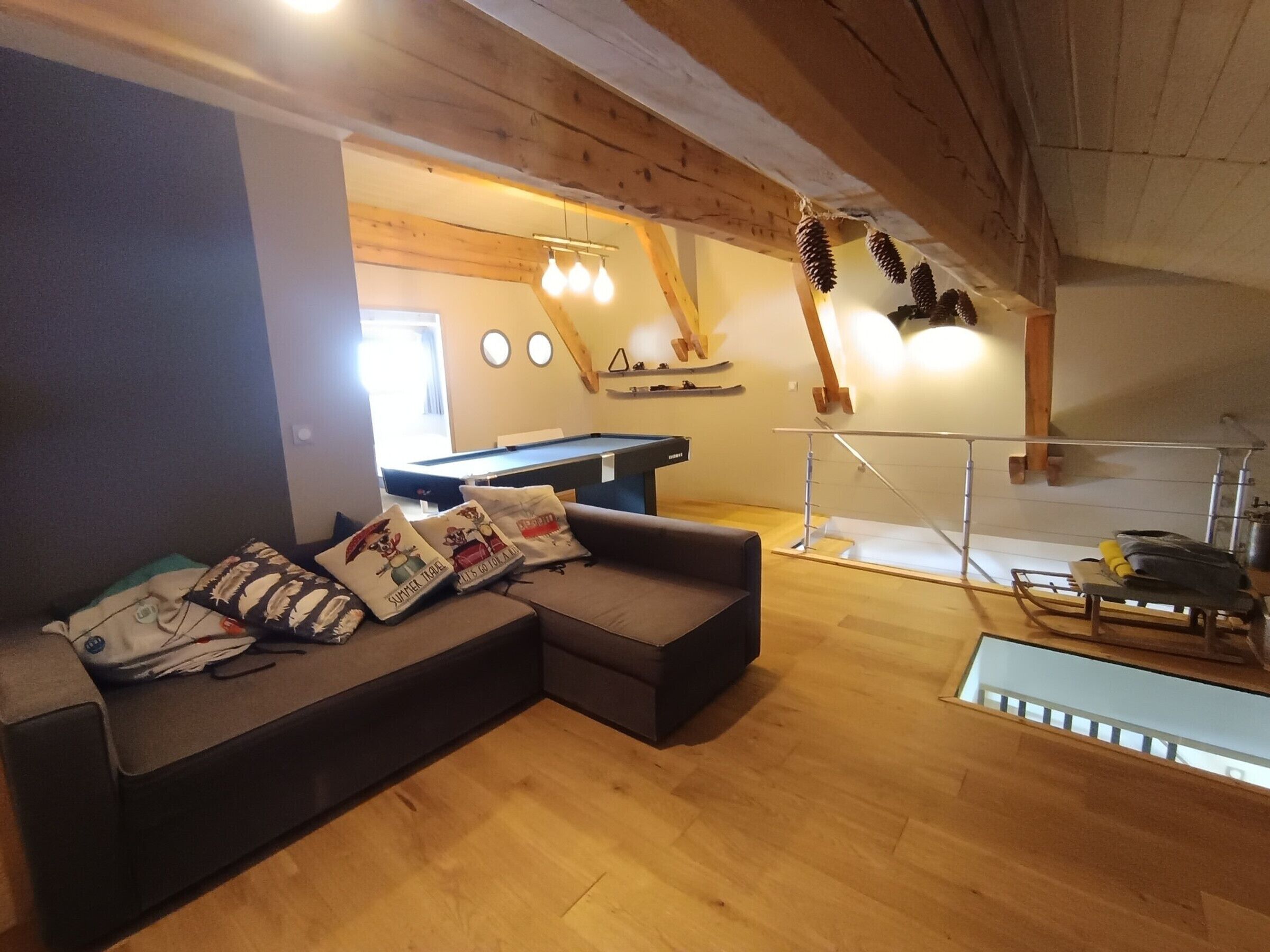 A cozy living room with a sectional sofa, a pool table, and a staircase leading to an upper level.