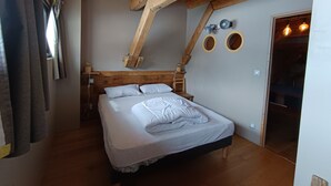 Quarto com teto de madeira, cama com roupa de cama branca, cabeceira de madeira e uma pequena mesa de cabeceira de madeira.
