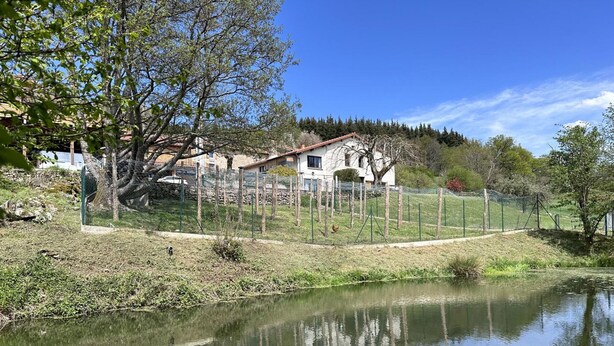 Une propriété paisible située au bord d’un lac, dotée d’un jardin clôturé, d’un étang et d’une maison à toit rouge.
