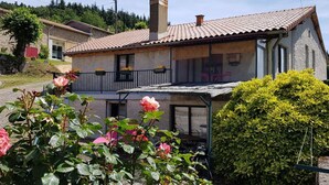 Une maison à deux étages, avec un toit en tuiles, une cheminée et un balcon agrémenté de plantes en pot.
