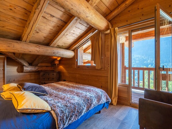 Une chambre à coucher aménagée dans une cabane en bois, avec un lit, des oreillers, une commode et une grande fenêtre donnant sur l’extérieur.