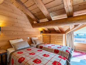 A cozy cabin room with two beds, wooden walls, and a sloped ceiling.