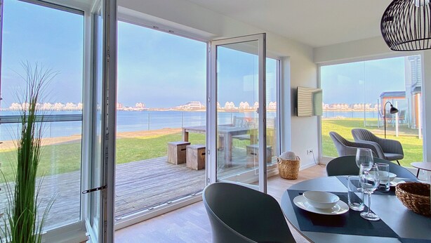 Uma área de jantar moderna com vista para o mar, uma porta de vidro deslizante e uma mesa posta para dois.