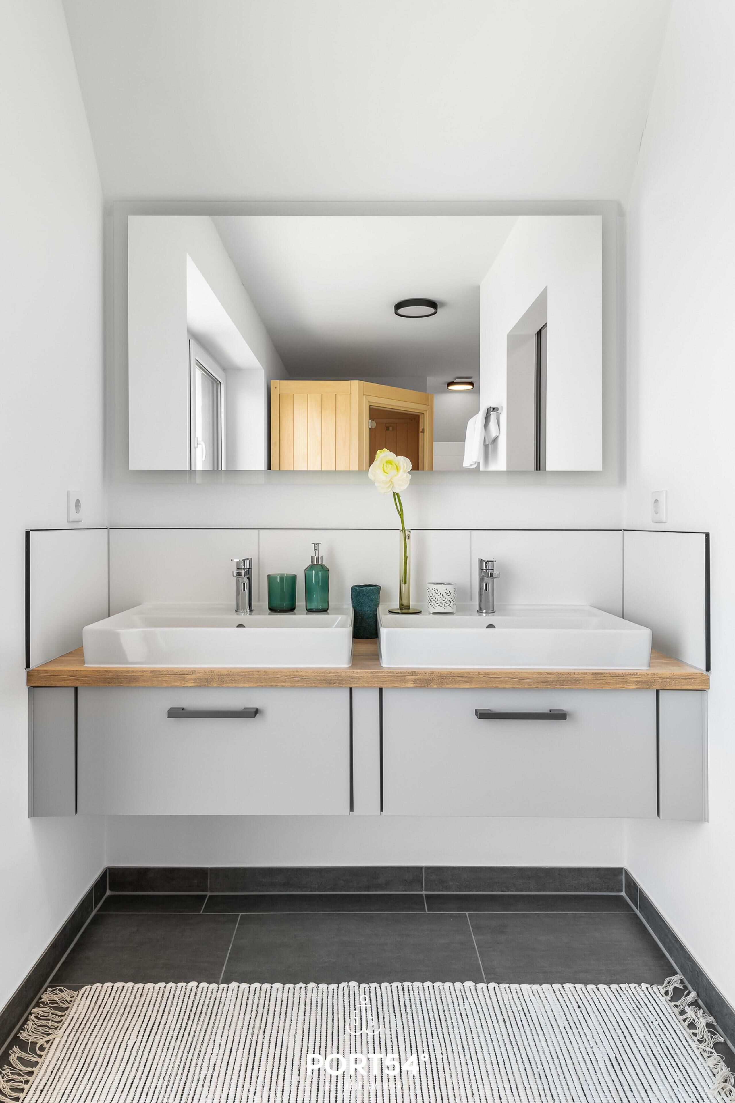 Een moderne badkamer met een grote spiegel, twee wastafels en een houten opbergmeubel.