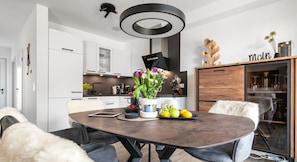 A modern kitchen with white cabinets, a dark wooden dining table, and a hanging light fixture. - Ferienhaus Wellenrauschen - Terrasse, Balkon, Sauna, Kamin, Nordsee- & Strandnah (Büsum)