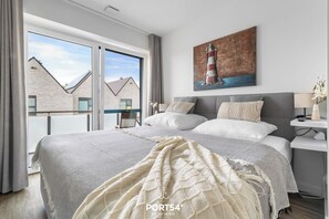 Een moderne slaapkamer met een groot bed, uitzicht op gebouwen en een schilderij van een vuurtoren.