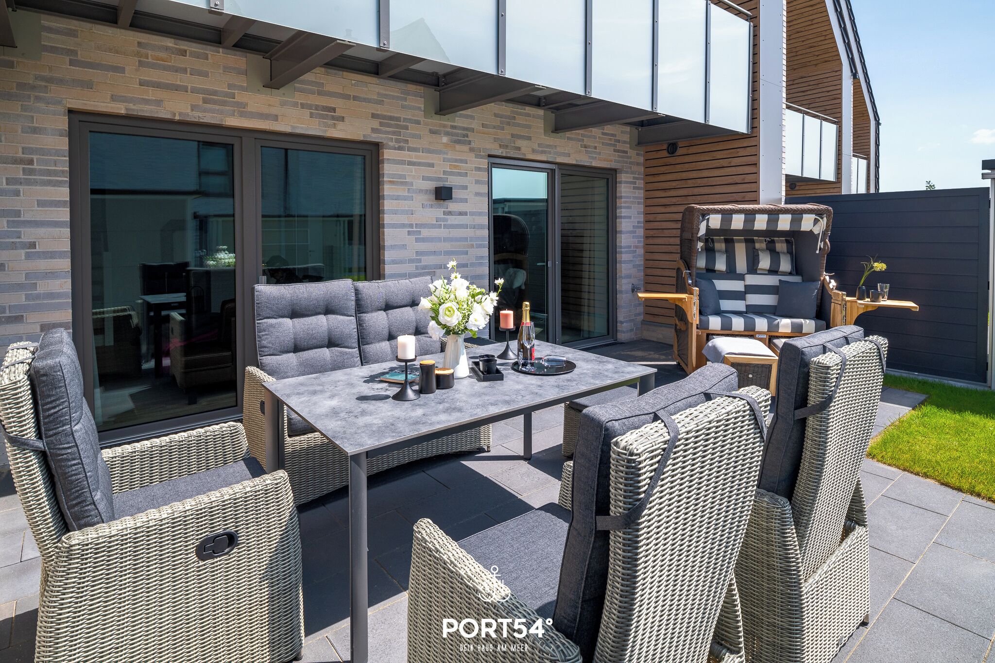 Un espace extérieur aménagé en terrasse, avec des meubles en osier, une table et une porte vitrée donnant accès à un espace intérieur.