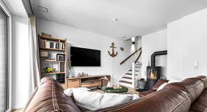 A modern living room with a brown leather sofa, a wooden entertainment unit, a flat-screen TV, and a fireplace. - Ferienhaus Wellenrauschen - Terrasse, Balkon, Sauna, Kamin, Nordsee- & Strandnah (Büsum)
