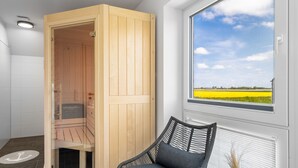 A sauna room with a wooden door, a chair, and a window with a view of a yellow field and wind turbines. - Ferienhaus Wellenrauschen - Terrasse, Balkon, Sauna, Kamin, Nordsee- & Strandnah (Büsum)