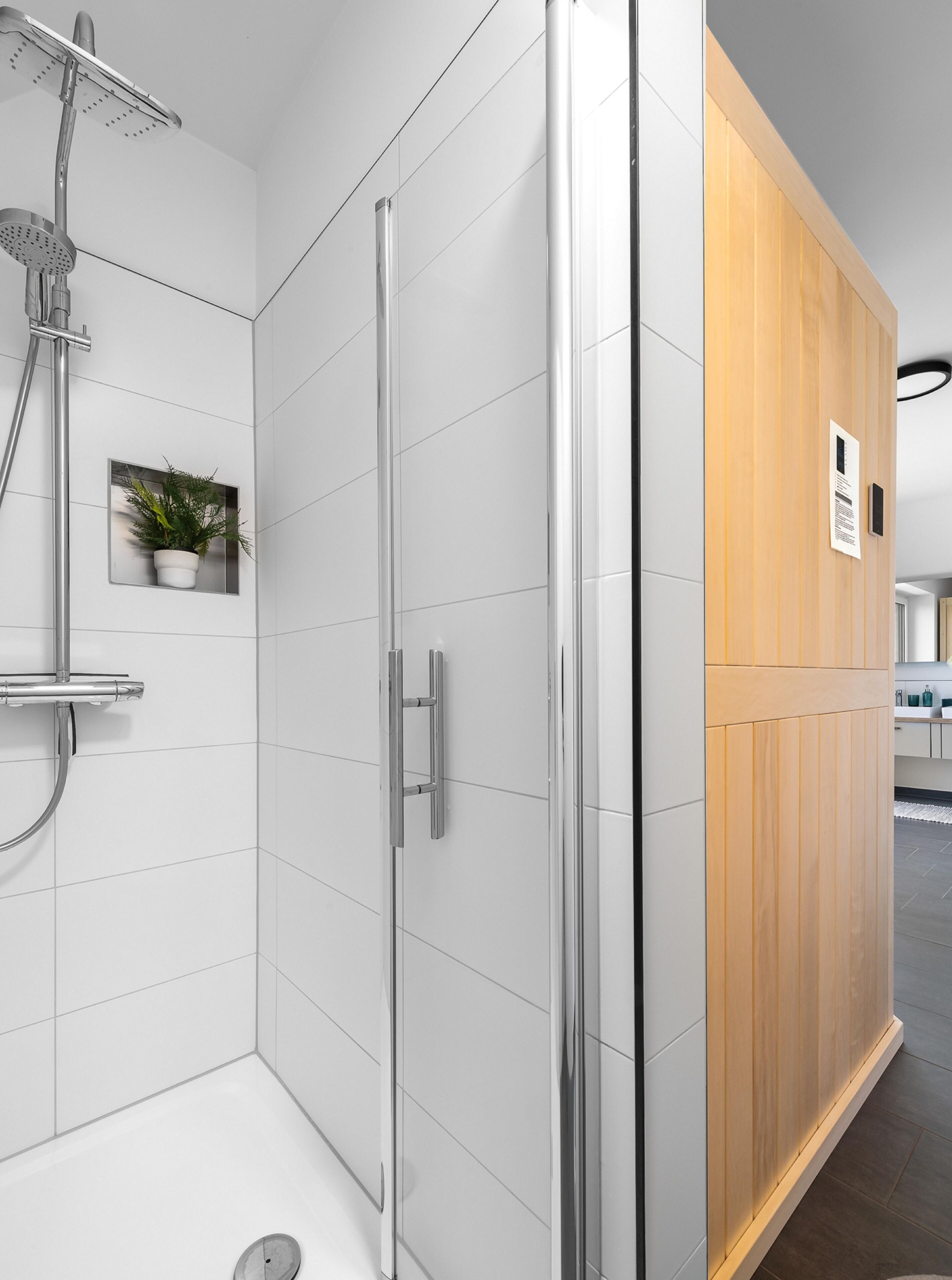 Ein modernes Badezimmer mit Duschkabine aus Glas, einer Wand aus Holzpaneelen und einem kleinen Topfpflanzen.