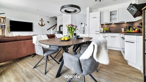 A modern kitchen with white cabinets, a round dining table, and a grey sofa. - Ferienhaus Wellenrauschen - Terrasse, Balkon, Sauna, Kamin, Nordsee- & Strandnah (Büsum)