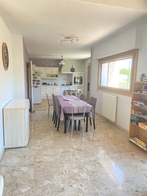 Een eetgedeelte met een tafel voor vier personen, een keuken op de achtergrond, en een raam dat natuurlijk licht binnenlaat.