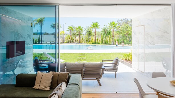 A modern living room with a glass wall, a pool, and outdoor furniture. - Lakes 24 at Praia da Falesia Vilamoura (Vilamoura)
