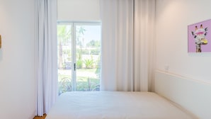 A bedroom with a bed, white curtains, a window with a view of greenery, and a giraffe painting on the wall. - Lakes 24 at Praia da Falesia Vilamoura (Vilamoura)