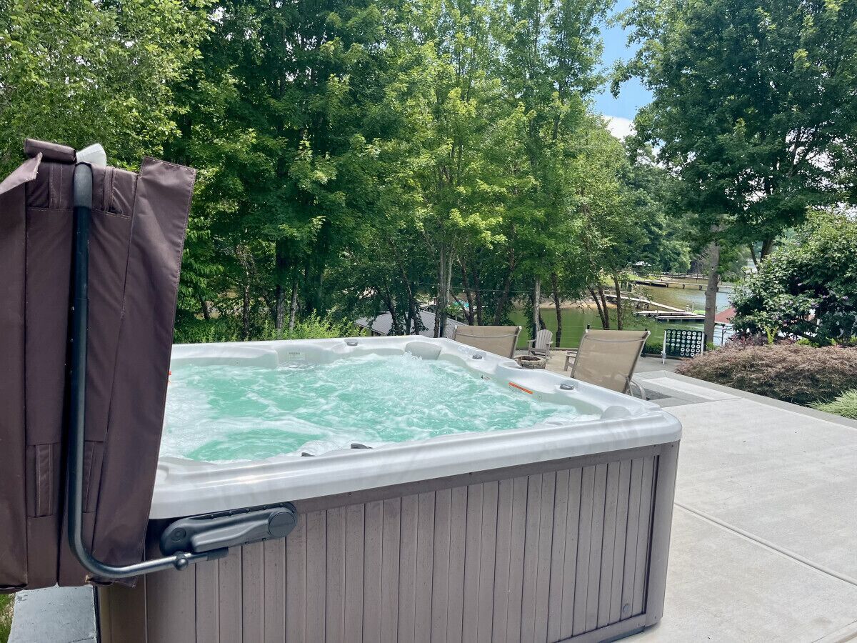 A hot tub with a cover, surrounded by a wooden deck and outdoor furniture.