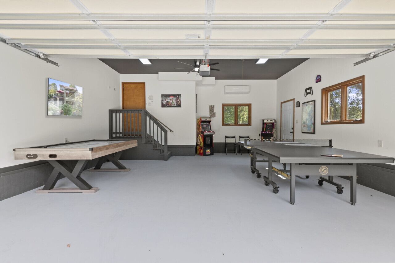 Un grand espace intérieur comprenant deux tables de ping-pong, un escalier et une petite borne d’arcade.