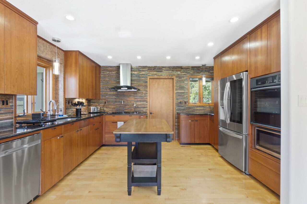A modern kitchen with wooden cabinets, a central island, stainless steel appliances, and a stone backsplash.