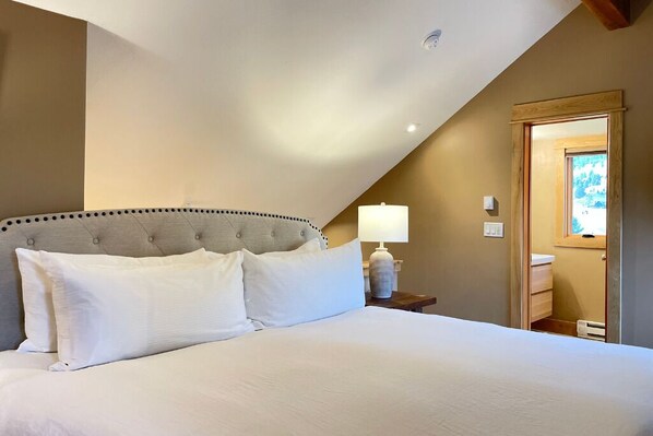 Ein Schlafzimmer mit einem großen Bett, einem Nachttisch mit Lampe und einer Holztür zu einem Badezimmer.