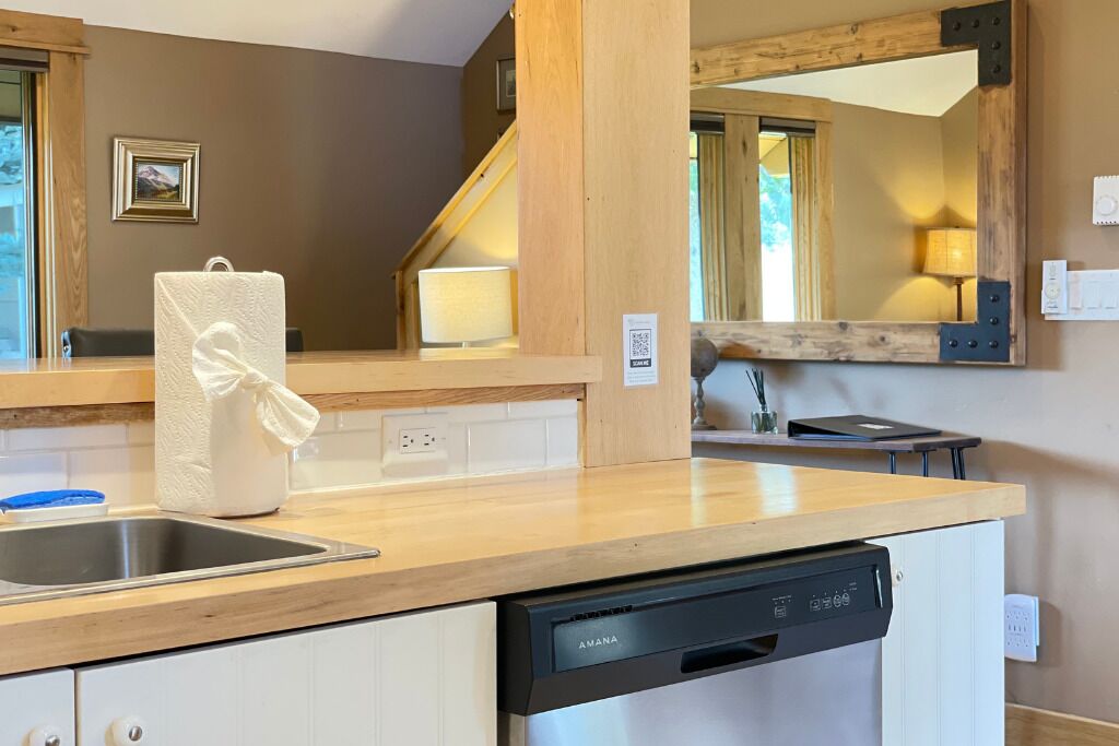 A kitchen with a wooden countertop, a dishwasher, a sink, and a mirror with a wooden frame.