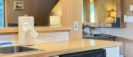 A kitchen with a wooden countertop, a dishwasher, a sink, and a mirror with a wooden frame.