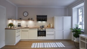 Moderni keittiö, jossa on valkoiset kaapit, sisäänrakennettu uuni ja ruostumattomasta teräksestä valmistettu liesituuletin.