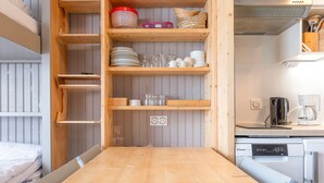 A compact kitchen with wooden shelves, a coffee maker, and a dishwasher.