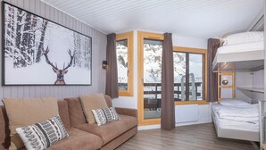 A cozy room with a brown sofa, a framed picture of a deer, a bunk bed, and a window with a view of snow-covered trees.