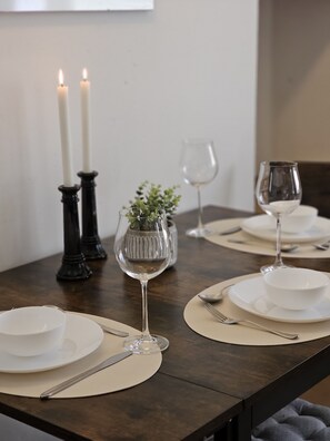 Una mesa de comedor dispuesta con platos, cuencos, cubiertos y copas de vino.